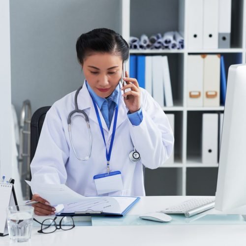 Asian medical specialist sitting at her table and calling to patient