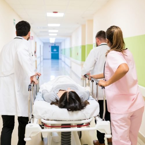 Doctors and nurse pushing female patient on stretcher at corridor in hospital
